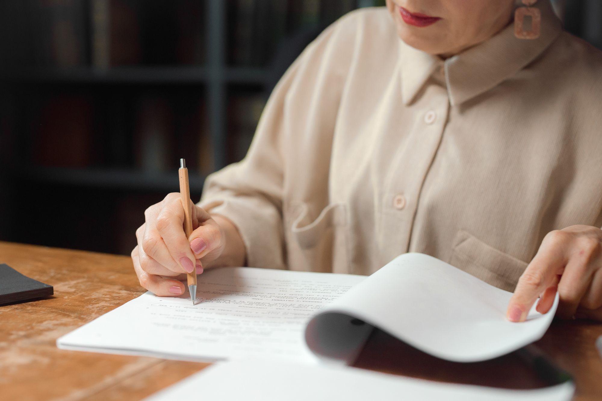 Close-up of someone marking up a printed document with a pencil at a wooden desk
