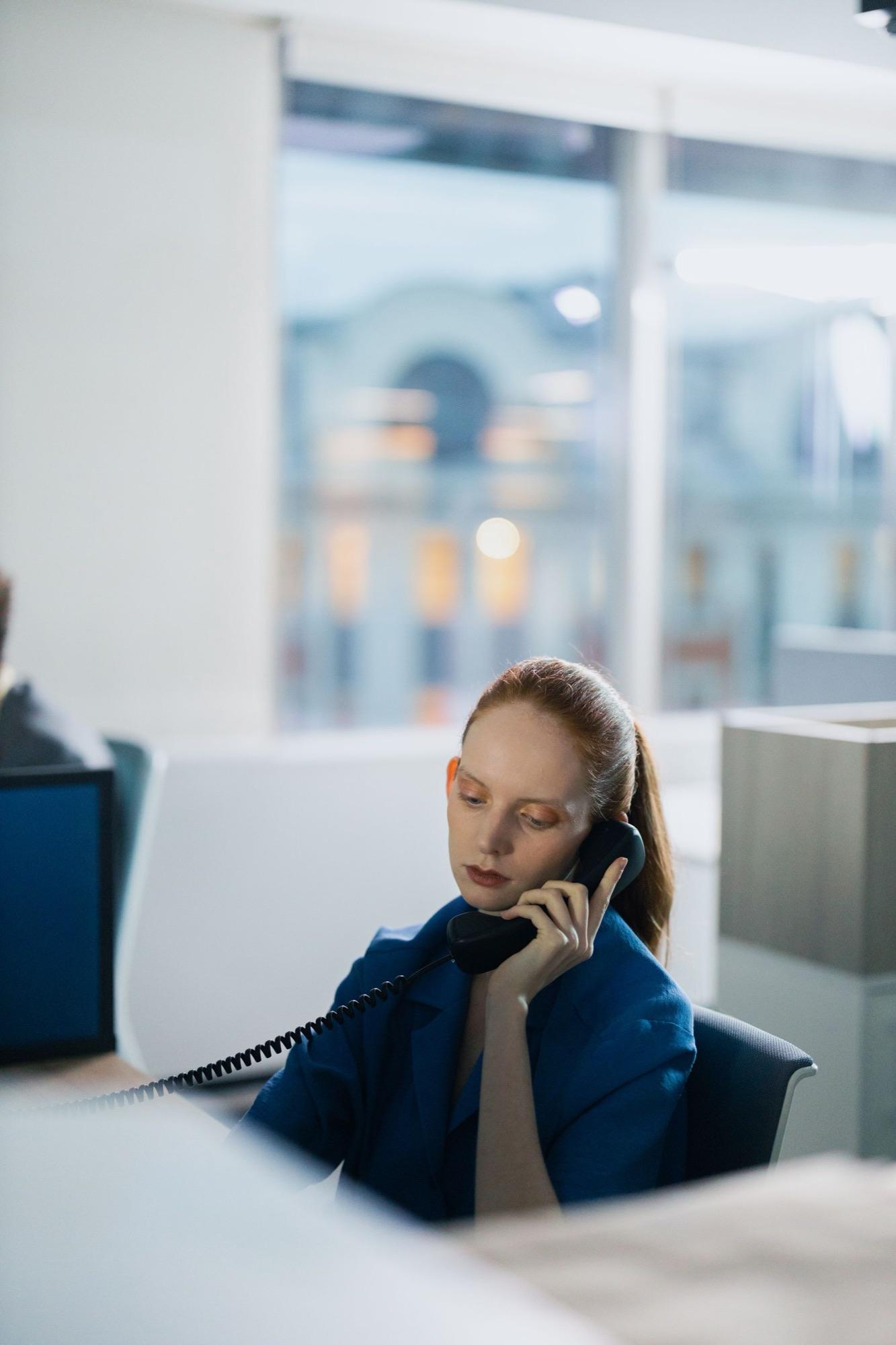 Coordinator in a blue blazer taking a call on a desk phone at a reception counter