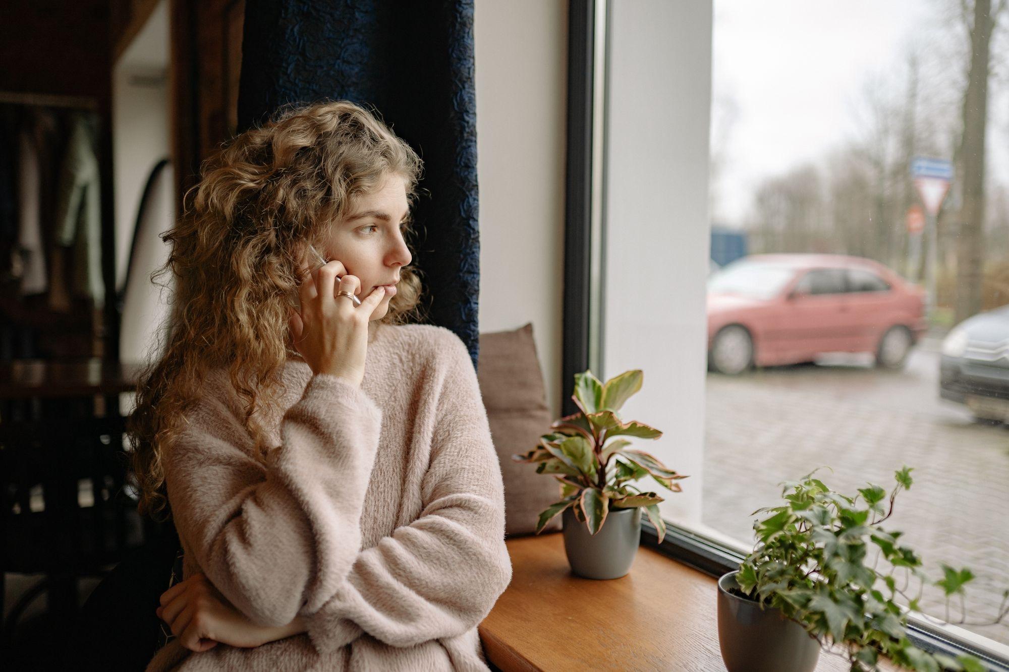 Person at home on the phone, looking out a window on an overcast day