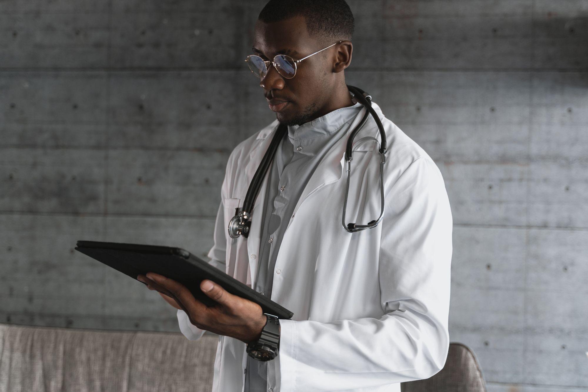 Provider in a white coat reading a chart on a tablet against a concrete wall