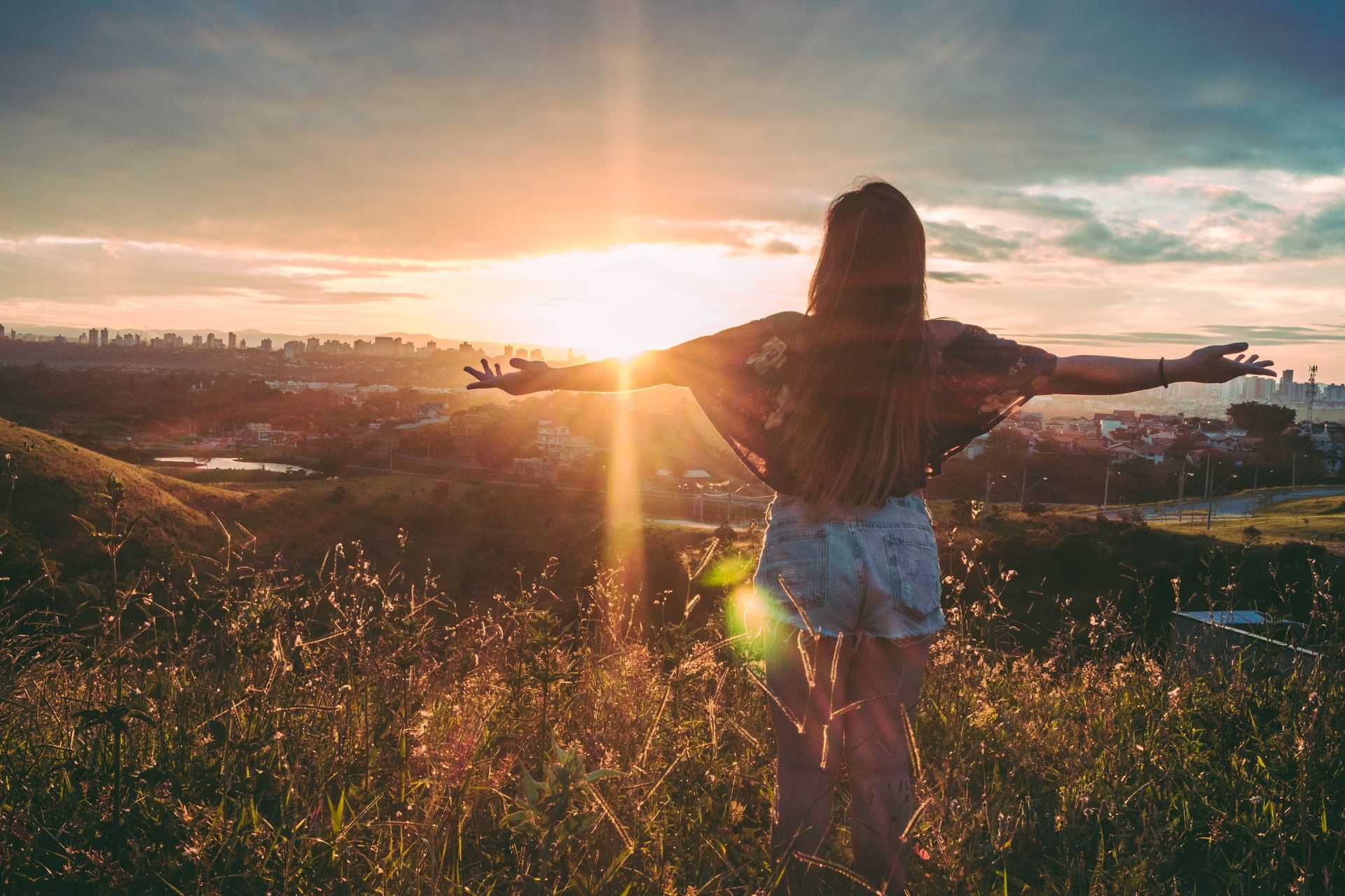 A person at sunrise overlooking the city, arms open in motion