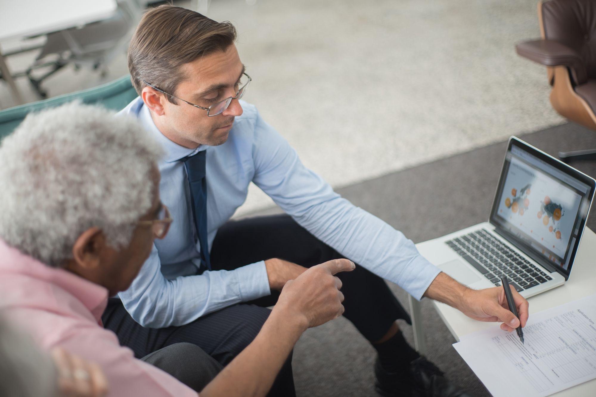 Advisor walking a client through a plan on a laptop and pointing to a printed form