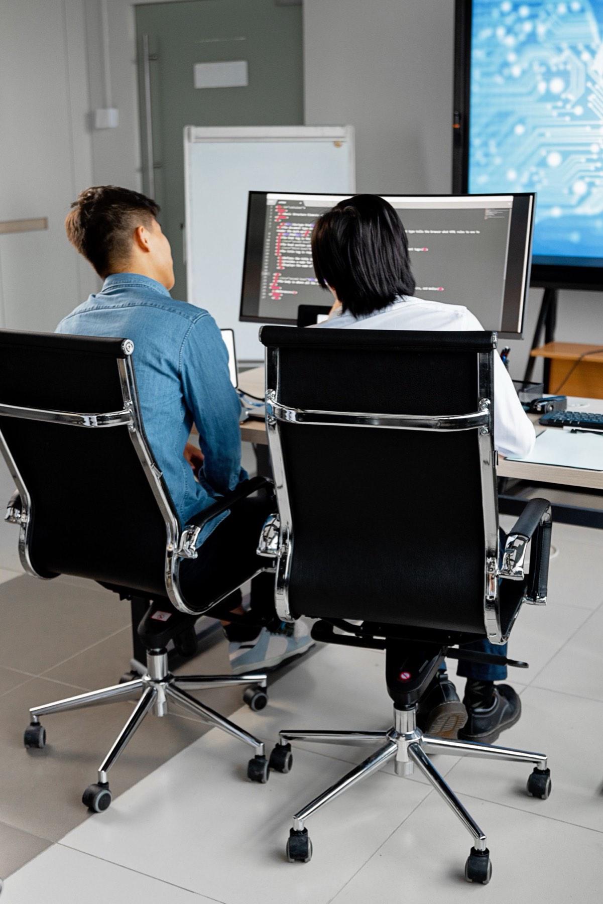 Two developers working through code together on a wide monitor