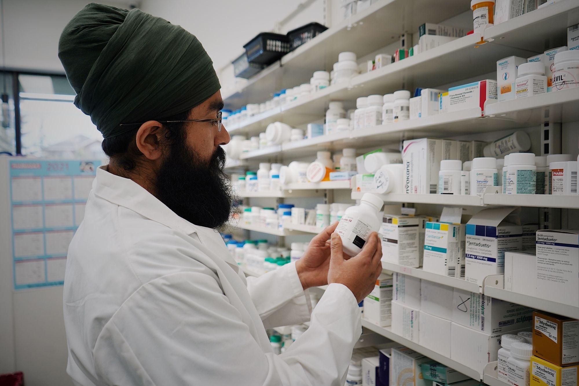 Pharmacist checking a medication bottle against shelf stock while preparing an order